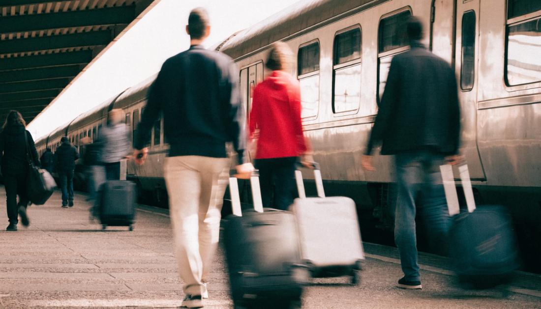Reisende mit Koffern gehen am Bahnsteig an einem stehenden Zug entlang