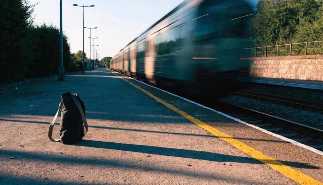 Ein Zug faehrt vom leeren Bahnsteig ab, im Vordergrund steht eine zurueckgelassene Tasche