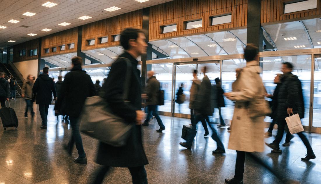 Pendler gehen mit Taschen durch eine belebte Bahnhofshalle
