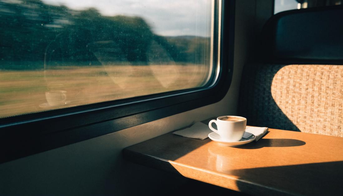 Weisse Kaffeetasse auf einem Tisch am Zugfenster, draussen zieht die Landschaft vorbei
