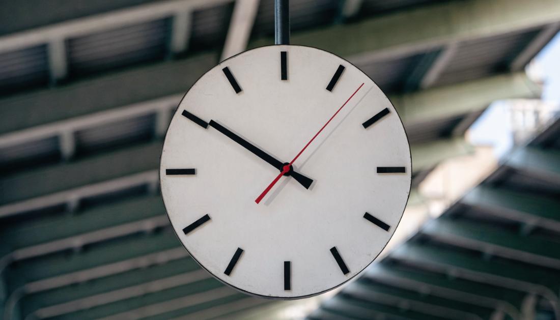 Grosse runde Bahnhofsuhr mit schlichtem Zifferblatt unter einem Bahnhofsdach