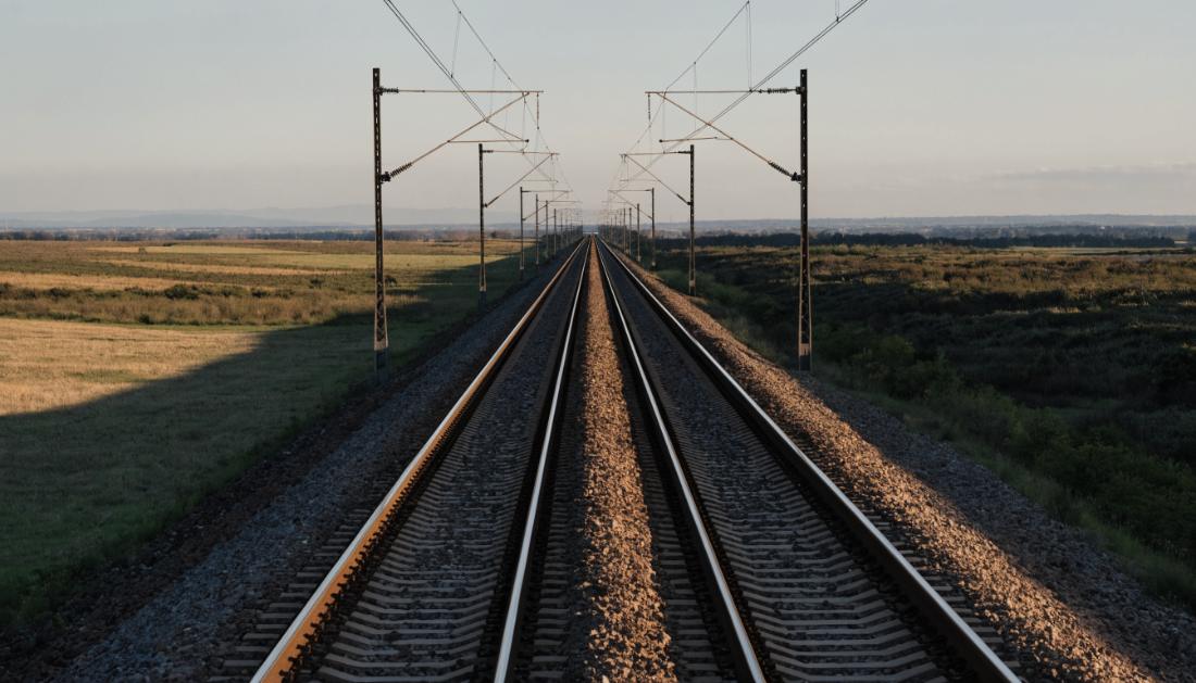 Gerade zweigleisige Bahnstrecke mit Oberleitungsmasten, die bis zum Horizont fuehrt