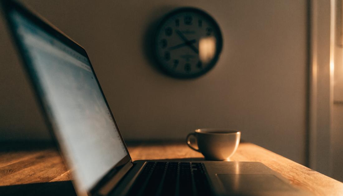 Laptop und Uhr auf einem Schreibtisch im warmen Abendlicht