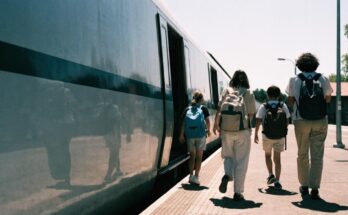 Zwei Erwachsene und zwei Kinder mit Rucksaecken steigen an einem sonnigen Bahnsteig in einen Zug