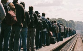 Eine groessere Gruppe Reisender mit Rucksaecken wartet gemeinsam auf dem Bahnsteig