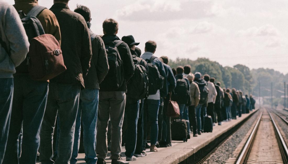 Eine gr&ouml;&szlig;ere Gruppe Reisender mit Rucks&auml;cken wartet gemeinsam auf dem Bahnsteig
