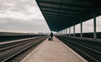 Ein Reisender mit Koffer steht allein auf einem leeren Umsteigebahnsteig