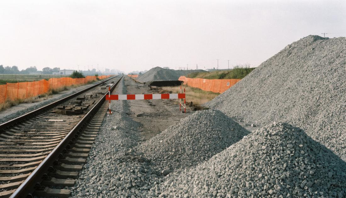 Eine gesperrte Bahnstrecke mit rot-wei&szlig;er Schranke, Bauzaun und frischem Schotter
