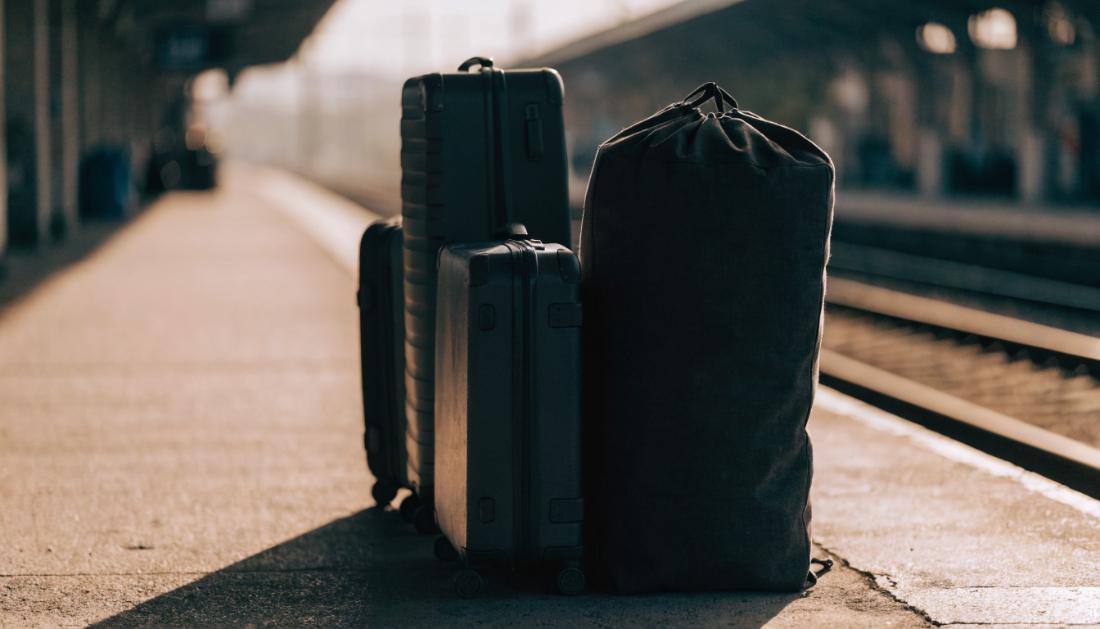 Mehrere Koffer und eine Reisetasche stehen im Morgenlicht auf einem Bahnsteig