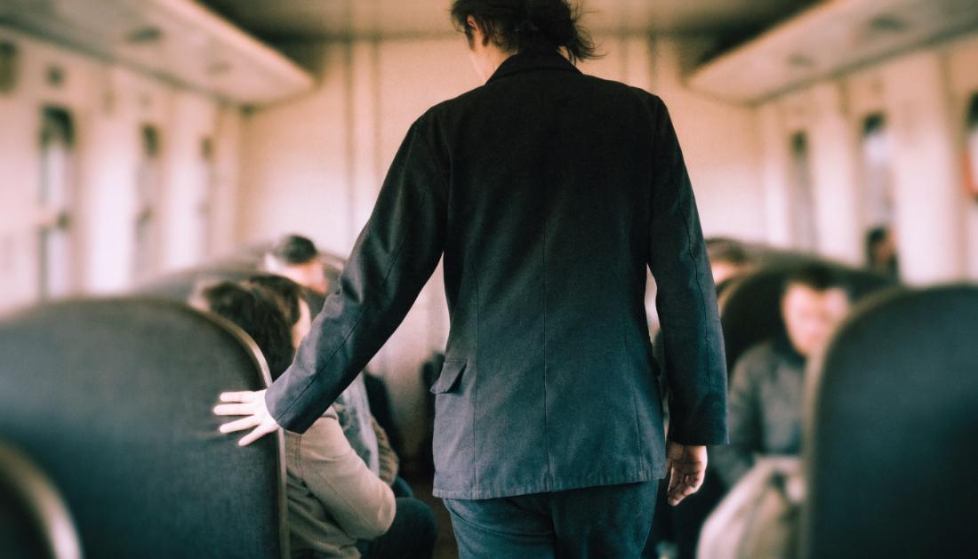 Ein Zugbegleiter in dunkler Uniform geht durch den Mittelgang eines Wagens