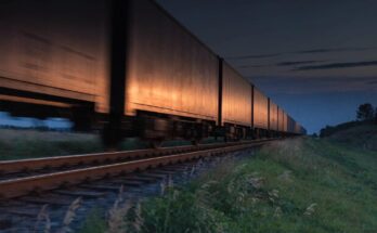 Langer Gueterzug mit Containerwagen faehrt in der Daemmerung durch die Landschaft