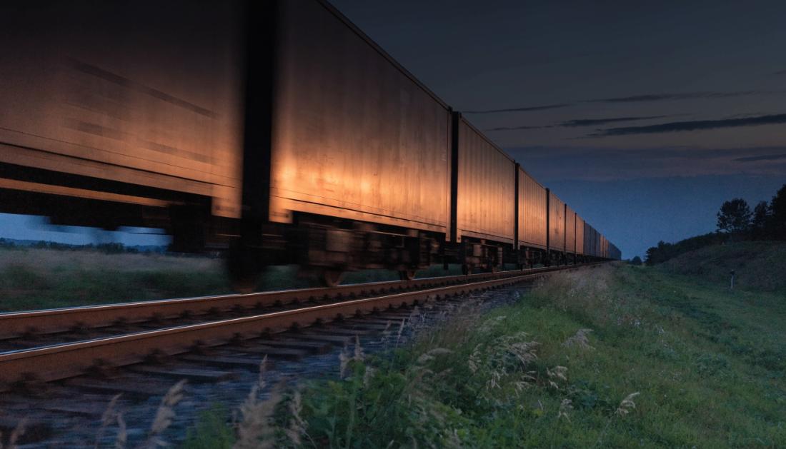 Langer G&uuml;terzug mit Containerwagen f&auml;hrt in der D&auml;mmerung durch die Landschaft