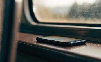 Ein Smartphone liegt auf einem Zugtisch, der Bildschirm leuchtet schwach