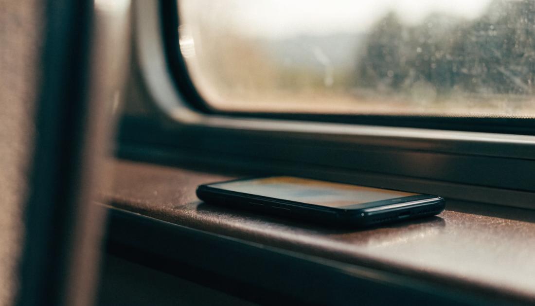 Ein Smartphone liegt auf einem Zugtisch, der Bildschirm leuchtet schwach