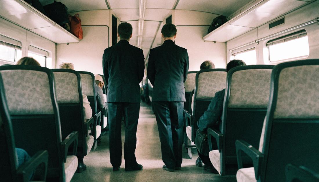 Zwei Kontrolleure in dunkler Kleidung stehen im Mittelgang eines Regionalzuges