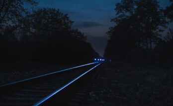 Blaues Licht spiegelt sich nachts in den Schienen einer leeren Bahnstrecke