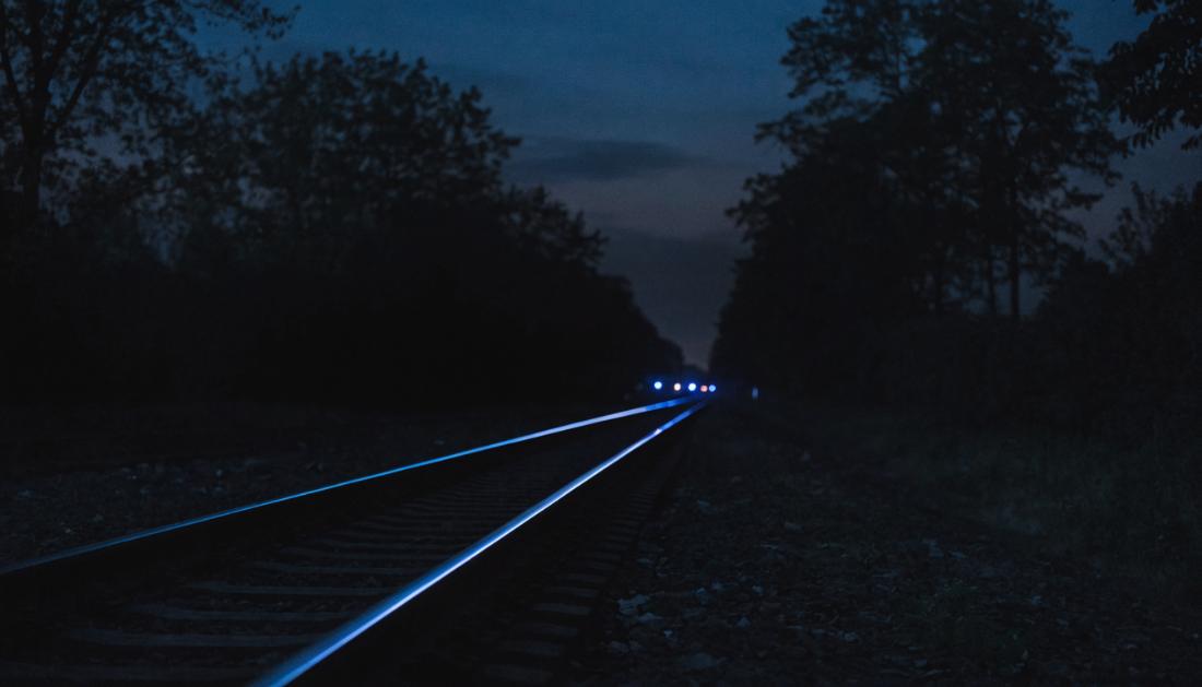 Blaues Licht spiegelt sich nachts in den Schienen einer leeren Bahnstrecke