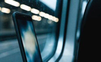 Ein Smartphone lehnt am Zugfenster, draussen verschwommene Lichter