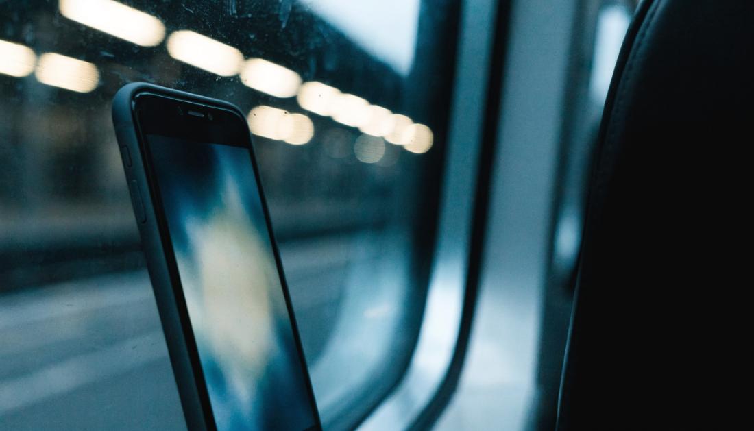 Ein Smartphone lehnt am Zugfenster, drau&szlig;en verschwommene Lichter