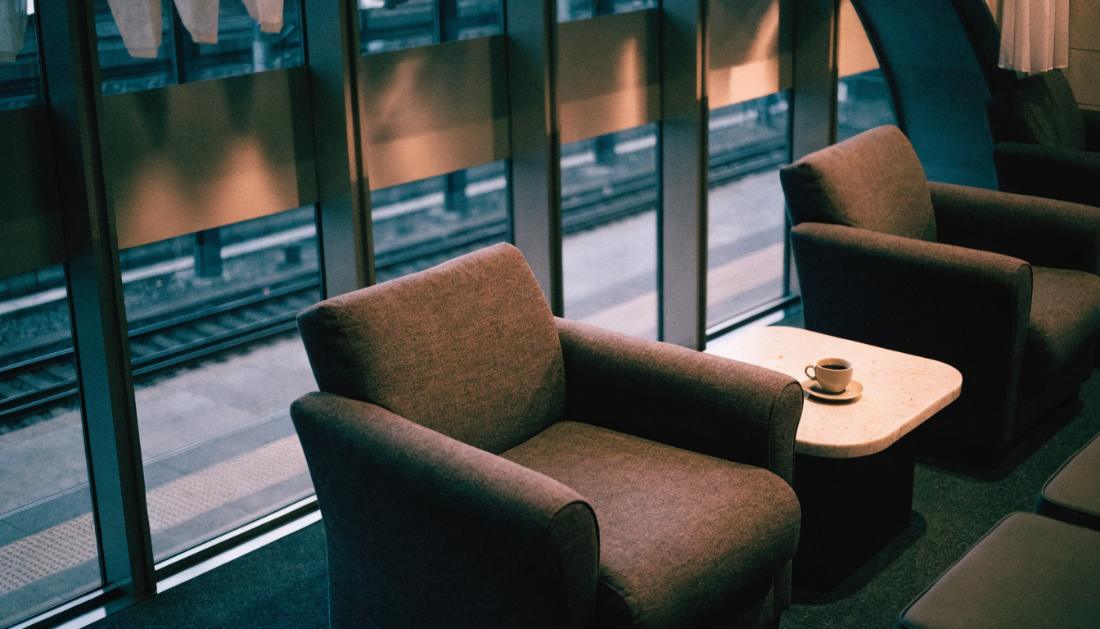 Sessel und niedriger Tisch in einer Lounge mit Fenstern zu den Bahnsteigen