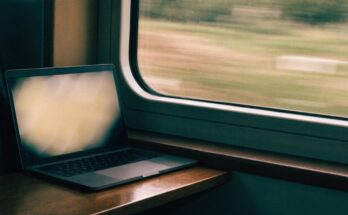 Ein aufgeklappter Laptop steht auf einem Zugtisch am Fenster