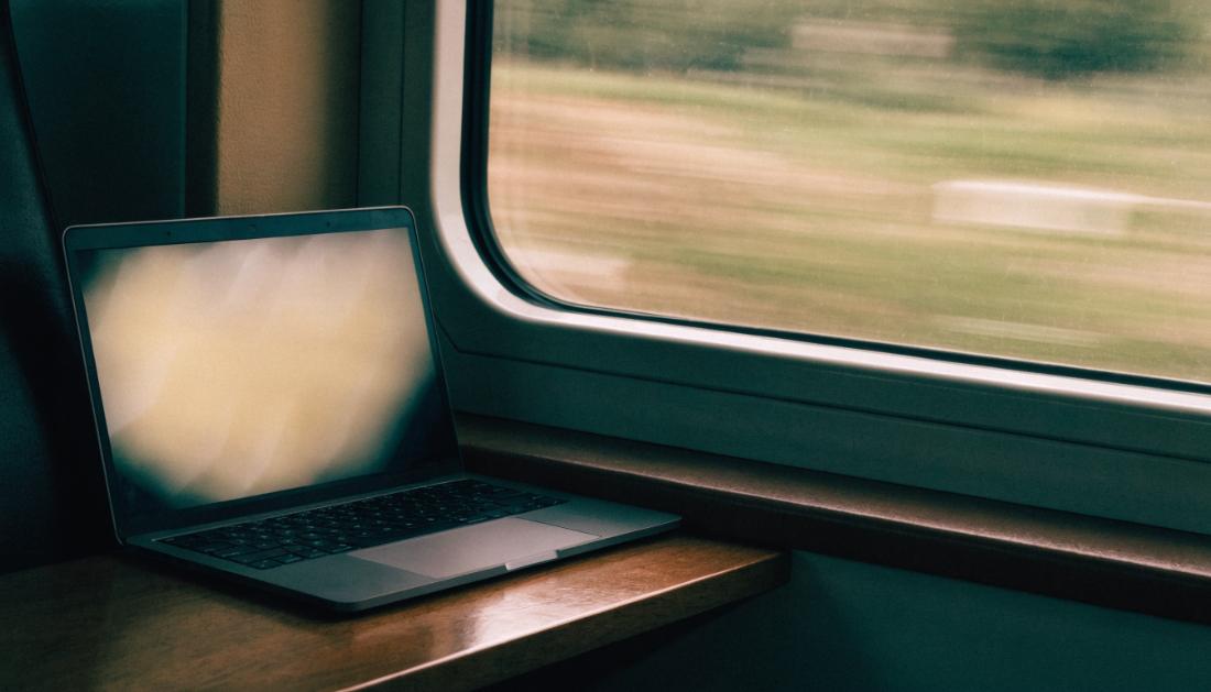 Ein aufgeklappter Laptop steht auf einem Zugtisch am Fenster