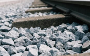 Nahaufnahme von Gleisschotter um eine Betonschwelle und den Schienenfuss