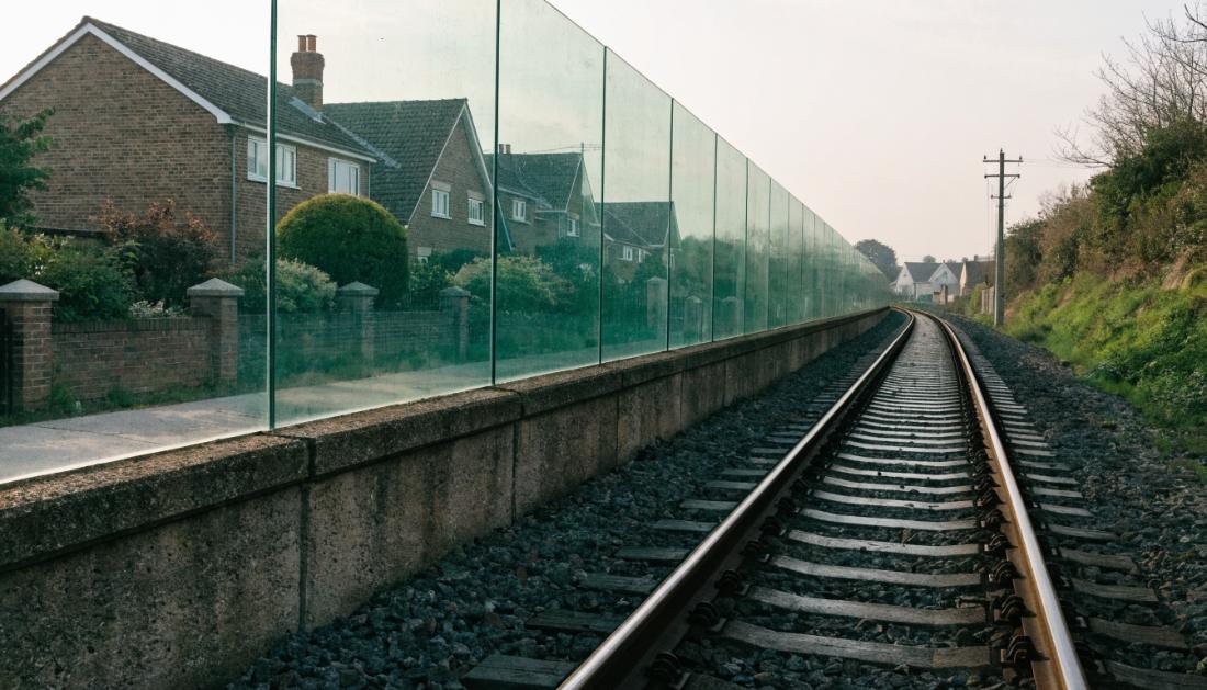 Eine hohe transparente Schallschutzwand trennt die Bahnstrecke von Wohnhäusern