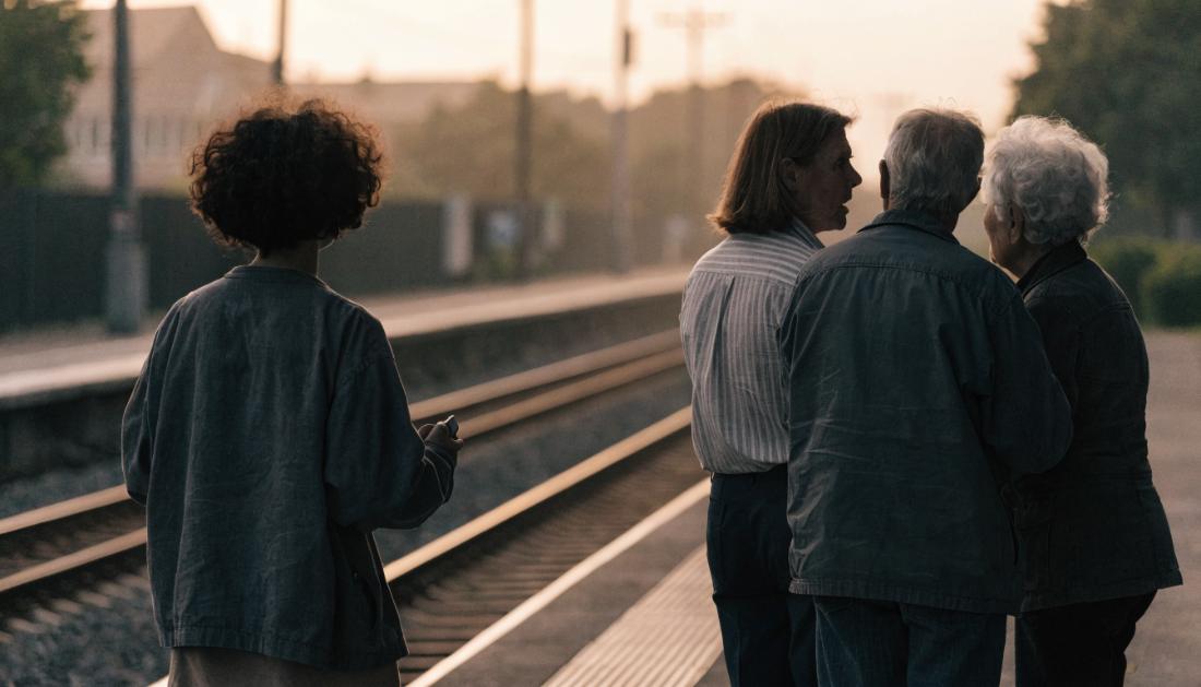 Mehrere Reisende stehen von hinten gesehen am Bahnsteig und unterhalten sich