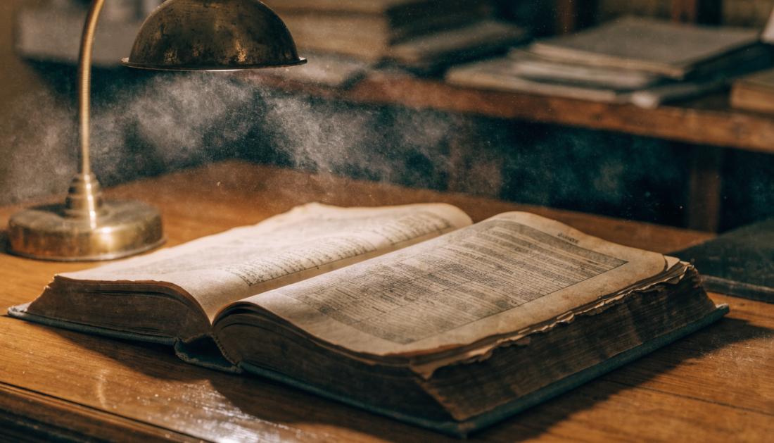 Ein dickes altes Buch liegt aufgeschlagen auf einem Holzschreibtisch