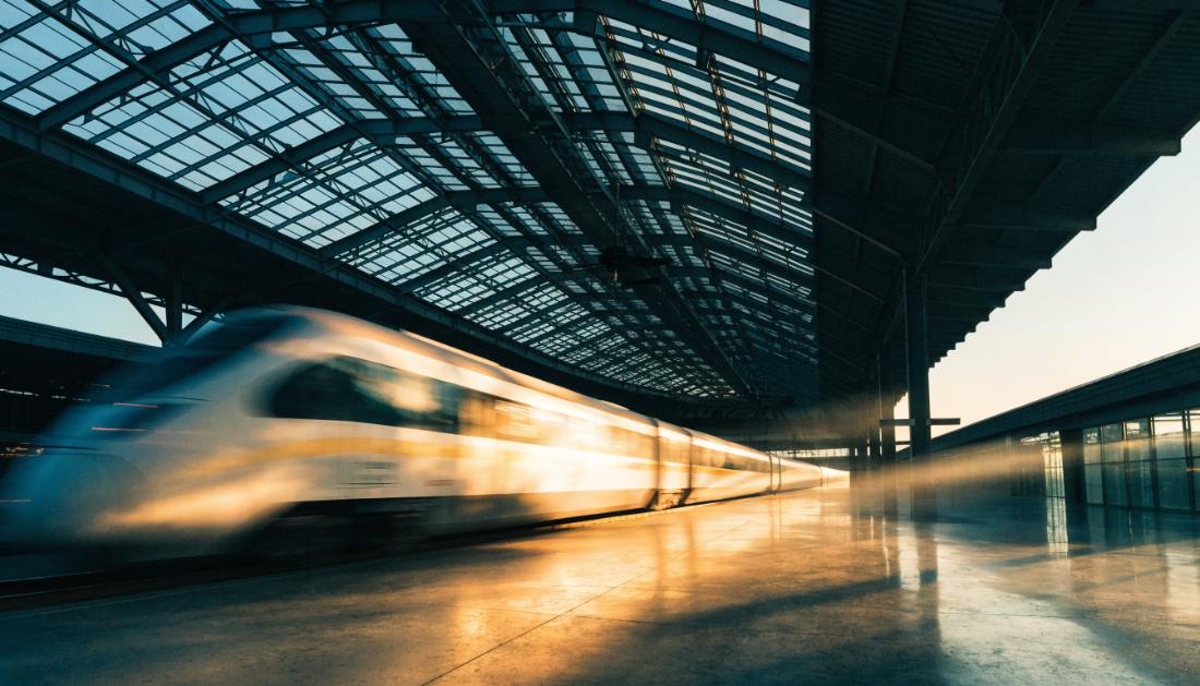 Ein moderner Schnellzug fährt in Bewegungsunschärfe aus einer gläsernen Bahnhofshalle