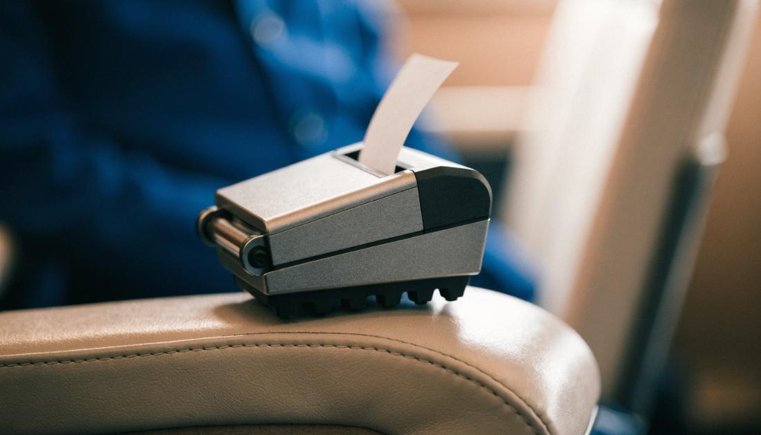 Ein kleines mobiles Fahrscheindruckgeraet liegt auf einer Zugsitzlehne