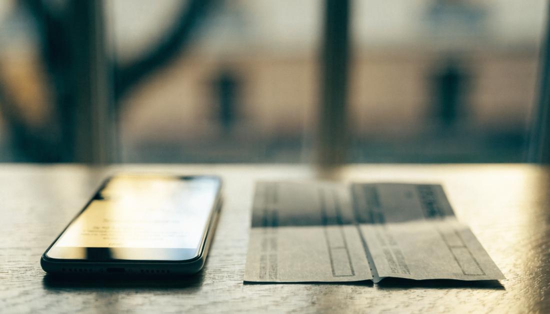 Ein Smartphone mit einer unscharfen Stornobestaetigung liegt neben einer gedruckten Fahrkarte