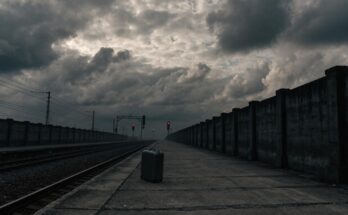 Ein einzelner verlassener Koffer steht auf einem leeren Bahnsteig, im Hintergrund rote Warnlichter