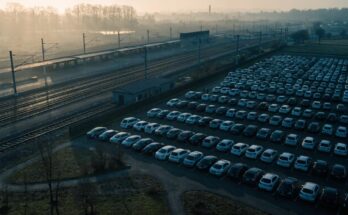 Luftaufnahme eines grossen Pendlerparkplatzes neben einem Bahnhof mit einem Zug im Hintergrund