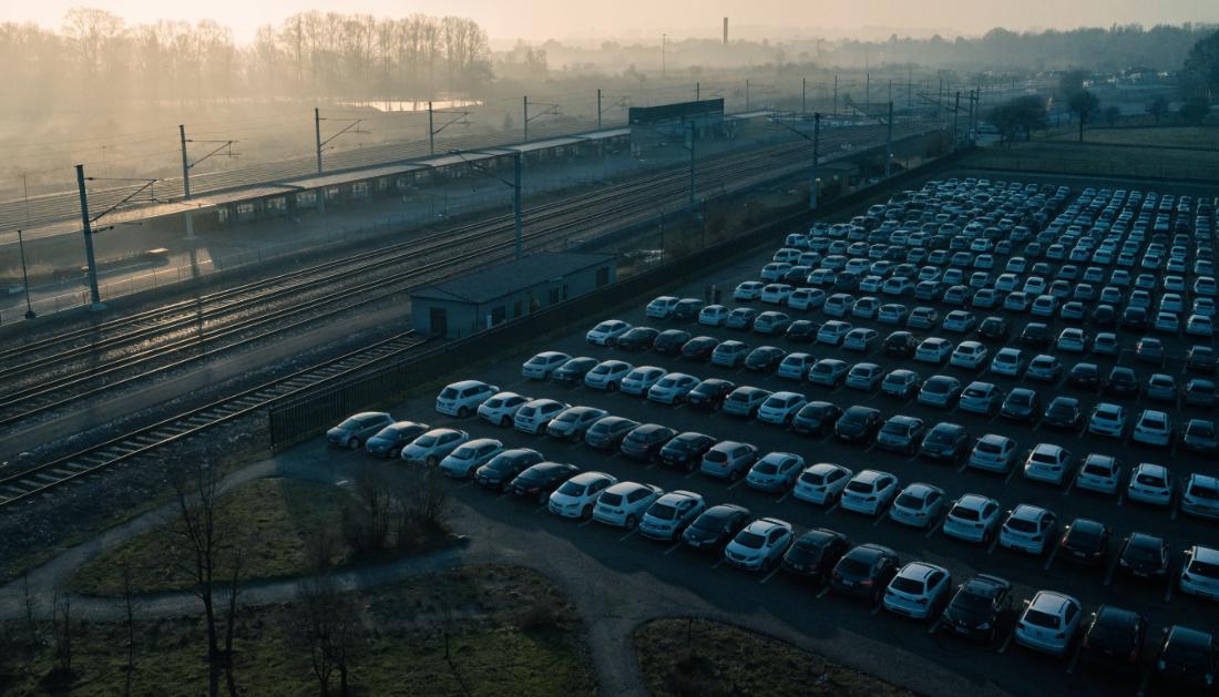 Luftaufnahme eines grossen Pendlerparkplatzes neben einem Bahnhof mit einem Zug im Hintergrund