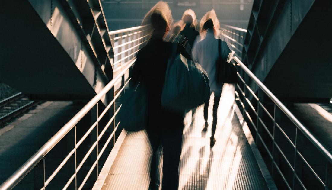 Reisende ueberqueren eilig eine Fussgaengerbruecke zwischen zwei Bahnsteigen