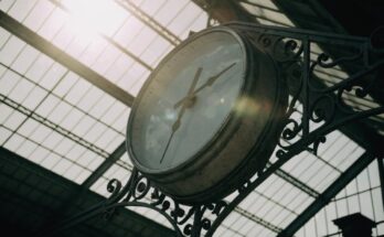 Eine grosse runde Bahnhofsuhr an einem eisernen Ausleger vor einer Glasdachkonstruktion
