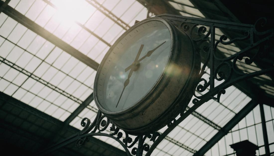 Eine grosse runde Bahnhofsuhr an einem eisernen Ausleger vor einer Glasdachkonstruktion