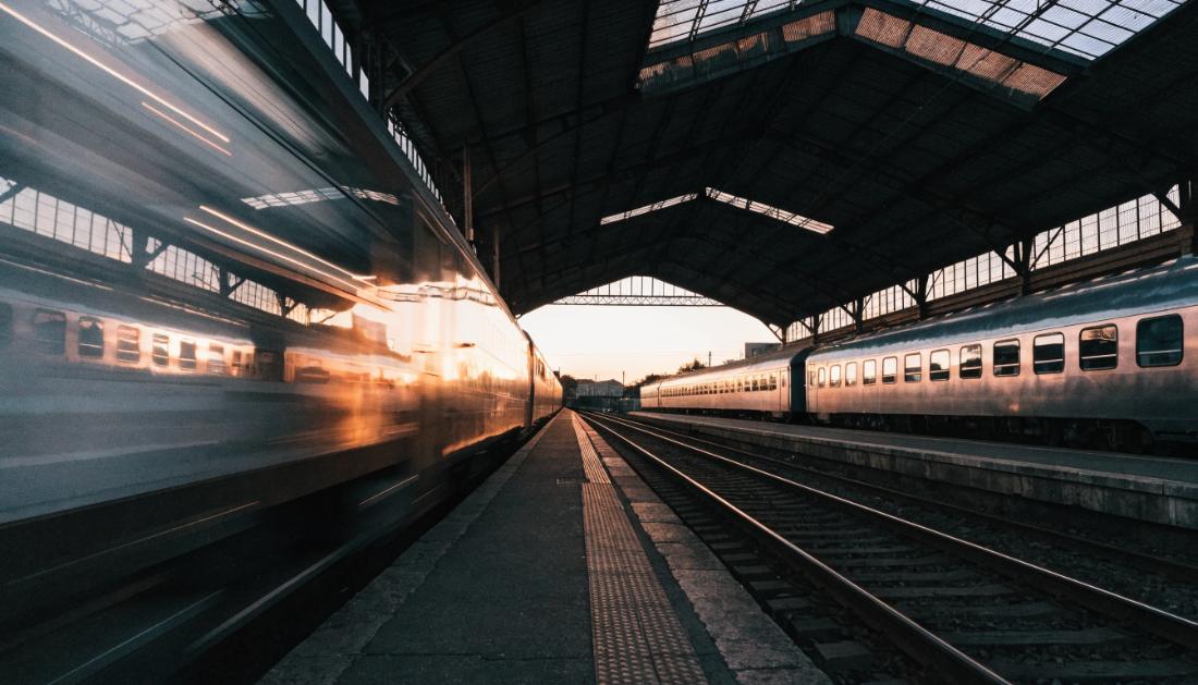 Zwei Zuege stehen an gegenueberliegenden Bahnsteigen, einer faehrt in Bewegungsunschaerfe ab