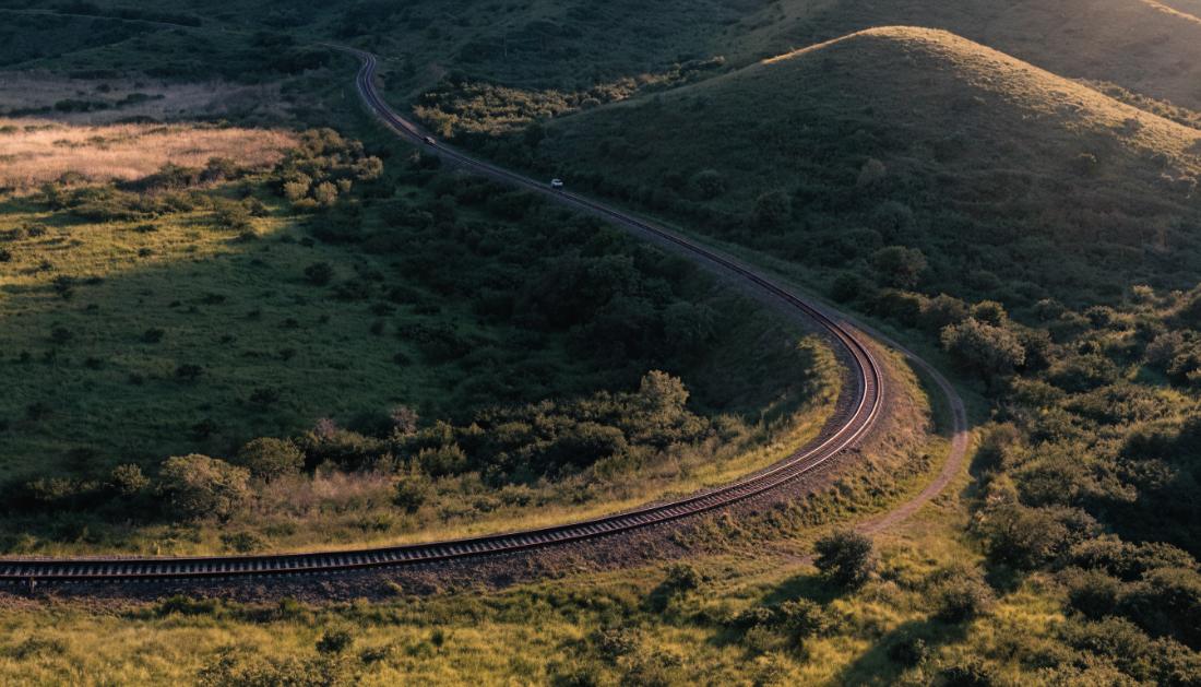Ein Bahngleis schwingt sichtbar geneigt durch eine Kurve in der Landschaft