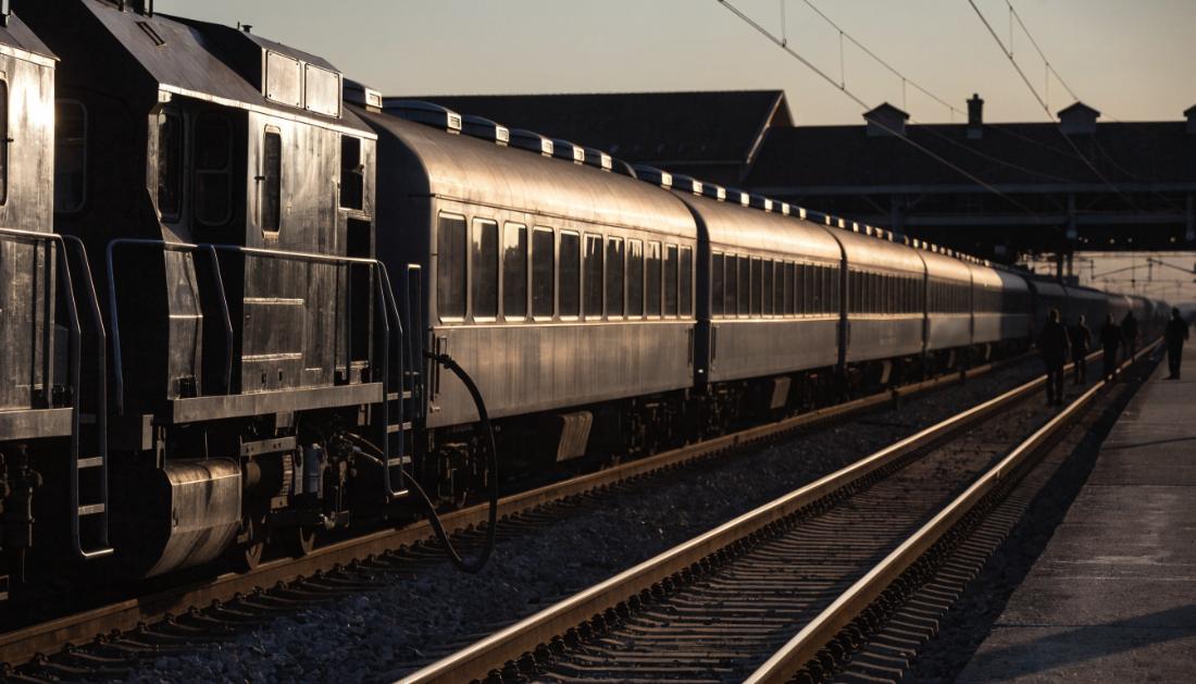 Eine Lokomotive wird von einer Wagenreihe abgekuppelt, im Hintergrund Silhouetten von Arbeitern