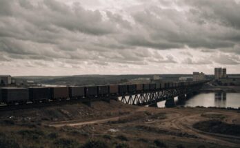 Ein langer Containerzug ueberquert eine Bruecke durch eine Industrielandschaft