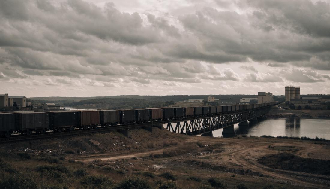 Ein langer Containerzug ueberquert eine Bruecke durch eine Industrielandschaft