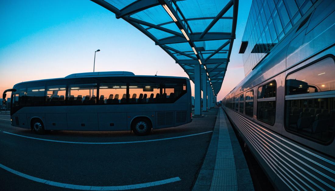 Ein Fernbus und ein Zug stehen nebeneinander an einem modernen Verkehrsknotenpunkt