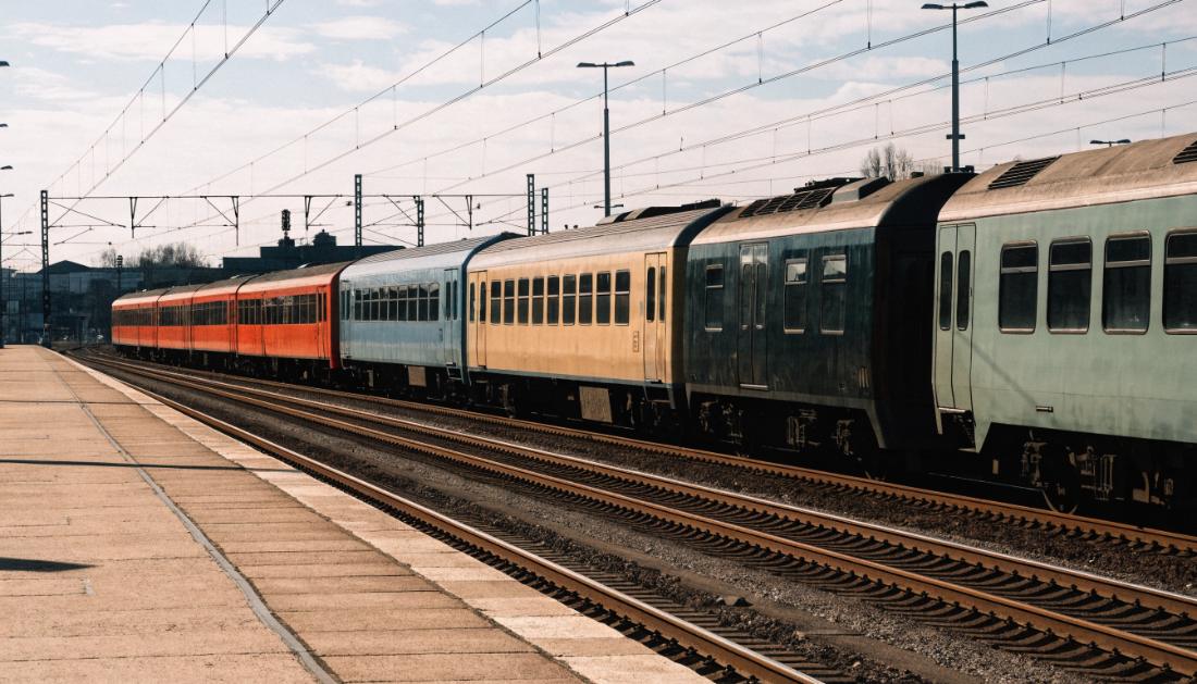 Mehrere unterschiedlich lackierte Regionalzuege stehen nebeneinander an einem grossen Bahnsteig