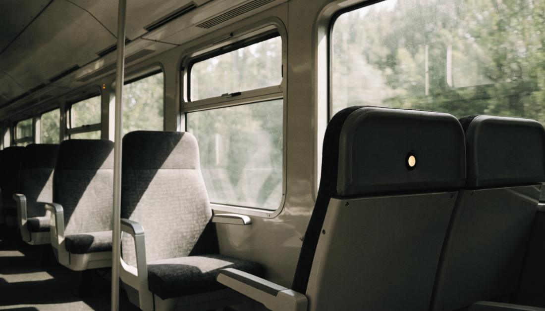 Ein halb besetzter Zugwagen bei Tageslicht mit einer leuchtenden Reservierungsanzeige über einem Sitz