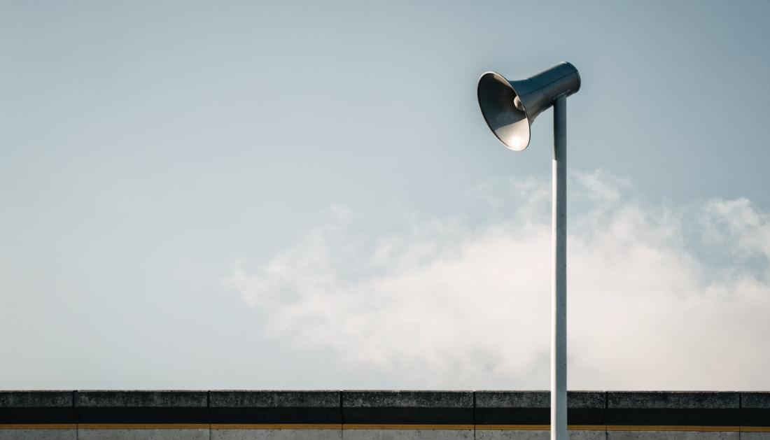 Ein Lautsprecher an einem Bahnsteigmast vor bewölktem Himmel
