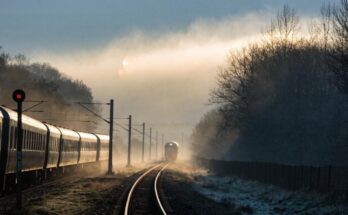 Ein Zug wartet vor einem Signal, während im Nebel ein weiterer Zug auf derselben Strecke sichtbar ist