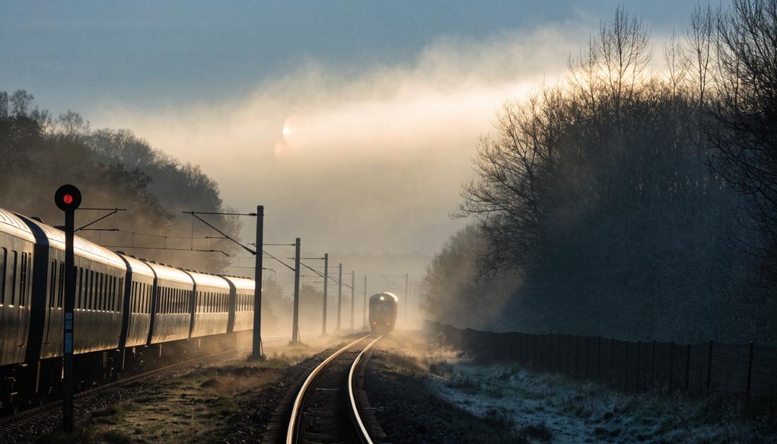 Ein Zug wartet vor einem Signal, während im Nebel ein weiterer Zug auf derselben Strecke sichtbar ist